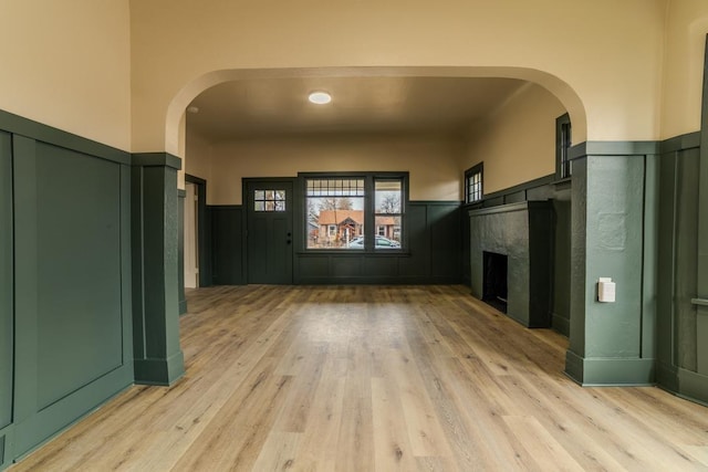 foyer with light wood finished floors, a wainscoted wall, arched walkways, and a high end fireplace