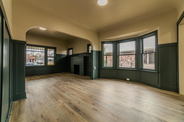 unfurnished living room with arched walkways, wainscoting, wood finished floors, and a premium fireplace