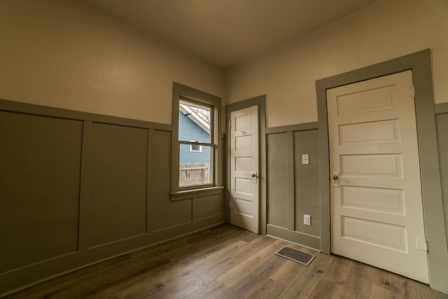 unfurnished bedroom with a decorative wall, wood finished floors, visible vents, and wainscoting