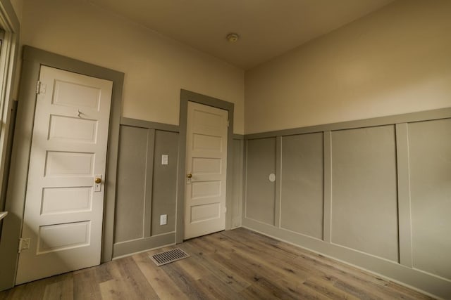 unfurnished bedroom featuring wood finished floors, a wainscoted wall, visible vents, a closet, and a decorative wall