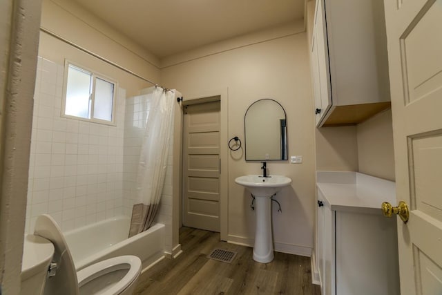 bathroom featuring visible vents, toilet, wood finished floors, shower / bath combination with curtain, and baseboards