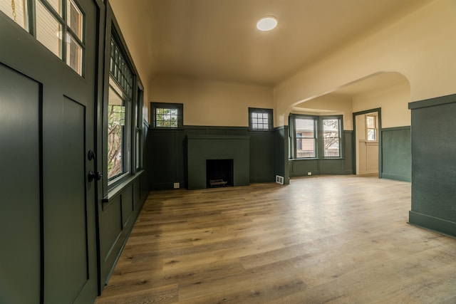 unfurnished living room with visible vents, a wainscoted wall, a fireplace, wood finished floors, and arched walkways