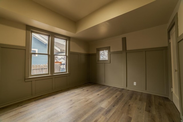 unfurnished bedroom with a decorative wall, light wood-style flooring, and a wainscoted wall