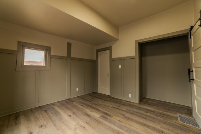 unfurnished bedroom with a wainscoted wall, visible vents, light wood-style flooring, a barn door, and a decorative wall