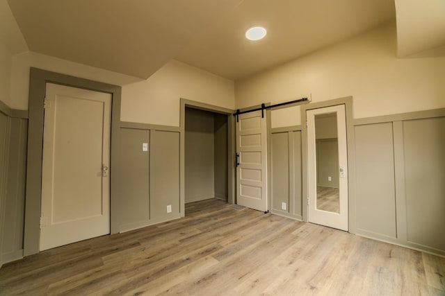 unfurnished bedroom with a barn door, multiple closets, light wood-style floors, and a decorative wall