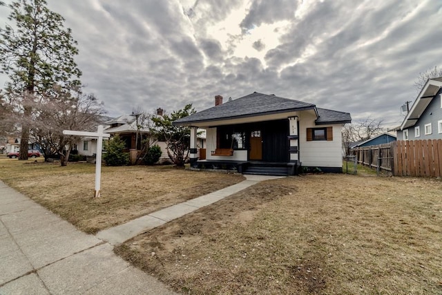 bungalow-style home featuring covered porch, a front lawn, and fence