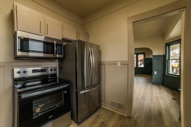 kitchen with visible vents, a wainscoted wall, appliances with stainless steel finishes, light wood-style floors, and arched walkways