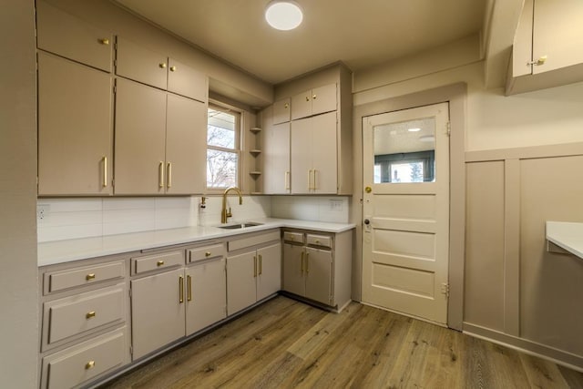 kitchen with open shelves, wood finished floors, light countertops, and a sink