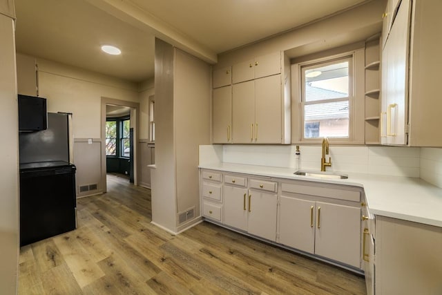 kitchen featuring visible vents, light wood-style flooring, a sink, tasteful backsplash, and light countertops