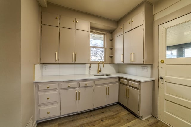 kitchen with a sink, backsplash, light countertops, wood finished floors, and open shelves