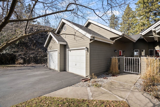 view of property exterior with a gate, fence, driveway, roof with shingles, and an attached garage