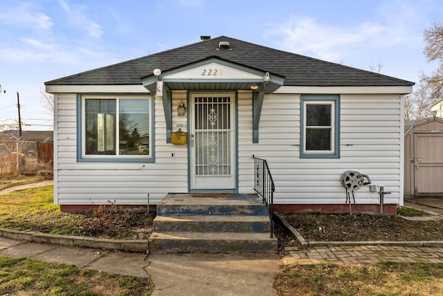 bungalow-style home with an outbuilding, a shed, and roof with shingles