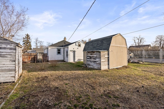 rear view of property featuring a shed, a fenced backyard, a gambrel roof, an outdoor structure, and a detached garage