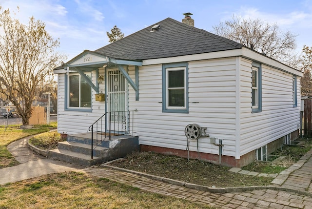 bungalow-style home featuring a chimney, roof with shingles, and fence