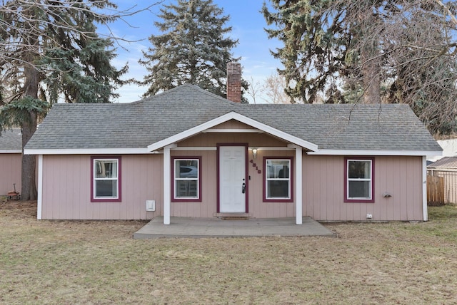 ranch-style house with a front lawn, roof with shingles, and a chimney