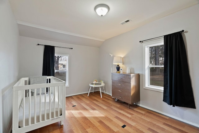 bedroom featuring visible vents, baseboards, a crib, and light wood finished floors