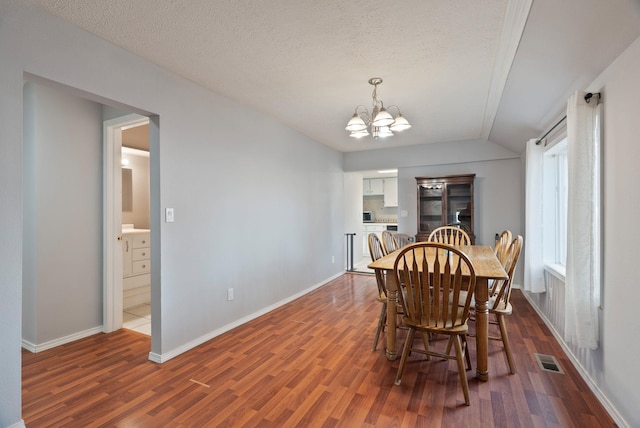 dining area with visible vents, a textured ceiling, a chandelier, dark wood-style flooring, and vaulted ceiling