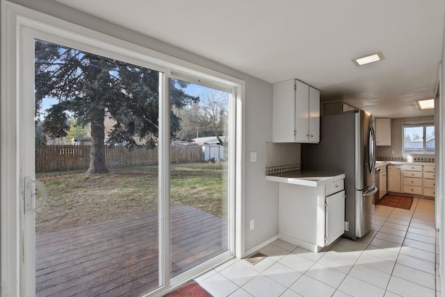 interior space featuring freestanding refrigerator, light countertops, light tile patterned floors, decorative backsplash, and baseboards