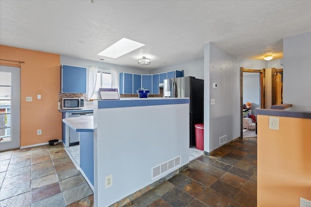 kitchen featuring stone tile floors, visible vents, appliances with stainless steel finishes, and blue cabinets