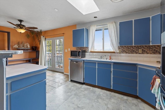 kitchen with blue cabinetry, backsplash, stainless steel appliances, a skylight, and light countertops