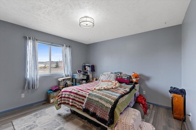 bedroom with wood finished floors, baseboards, and a textured ceiling