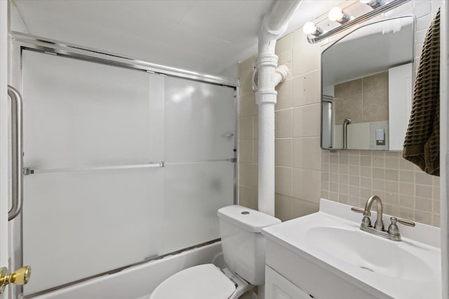 bathroom with toilet, tasteful backsplash, combined bath / shower with glass door, tile walls, and vanity