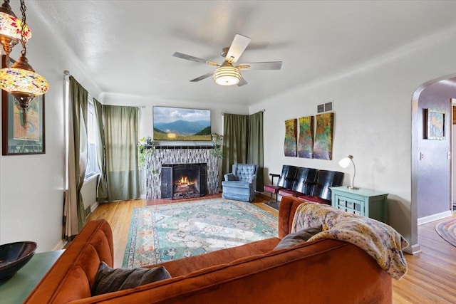 living room featuring visible vents, a warm lit fireplace, wood finished floors, arched walkways, and ceiling fan