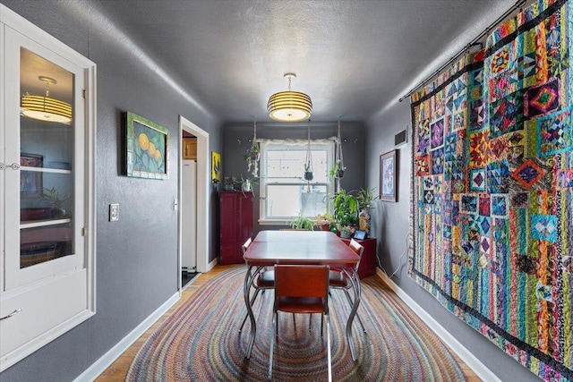 dining area featuring visible vents, a textured ceiling, baseboards, and wood finished floors