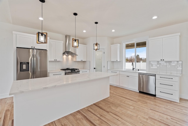 kitchen with light wood-type flooring, stainless steel appliances, white cabinetry, wall chimney exhaust hood, and a sink