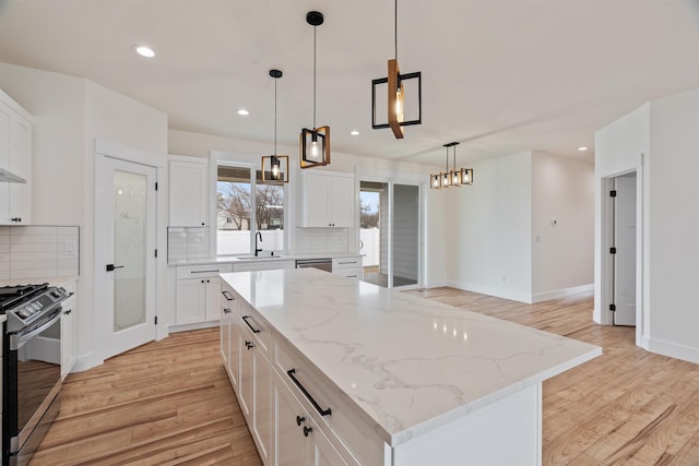 kitchen with decorative backsplash, gas range, light wood-style flooring, and white cabinetry