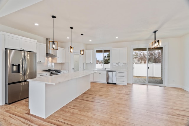 kitchen with light wood-type flooring, a kitchen island, white cabinetry, stainless steel appliances, and wall chimney range hood