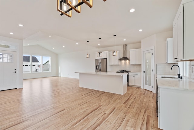 kitchen with wall chimney range hood, open floor plan, light wood-type flooring, appliances with stainless steel finishes, and a sink