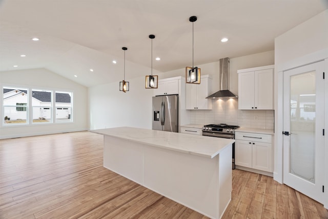 kitchen with a center island, white cabinetry, appliances with stainless steel finishes, wall chimney exhaust hood, and decorative backsplash