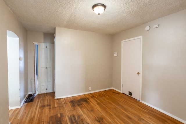 unfurnished room featuring baseboards, wood-type flooring, arched walkways, and a textured ceiling