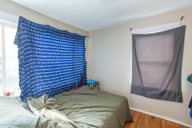 bedroom with wood finished floors, baseboards, and a textured ceiling