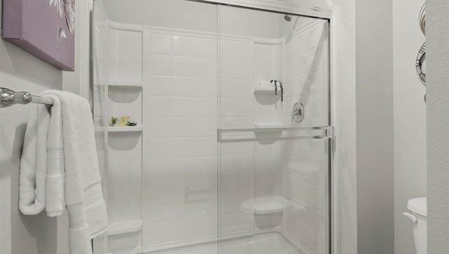 bathroom featuring toilet, a shower stall, and a textured wall