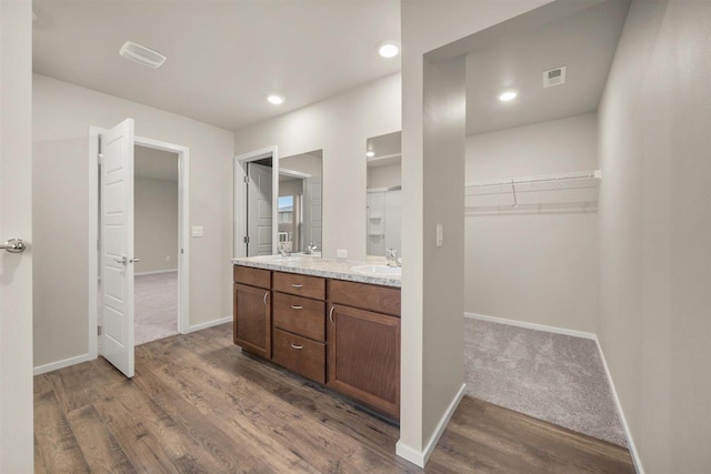 full bathroom featuring visible vents, a walk in closet, baseboards, double vanity, and wood finished floors