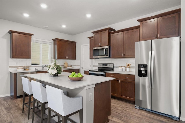 kitchen with a kitchen island, light countertops, wood finished floors, stainless steel appliances, and a sink