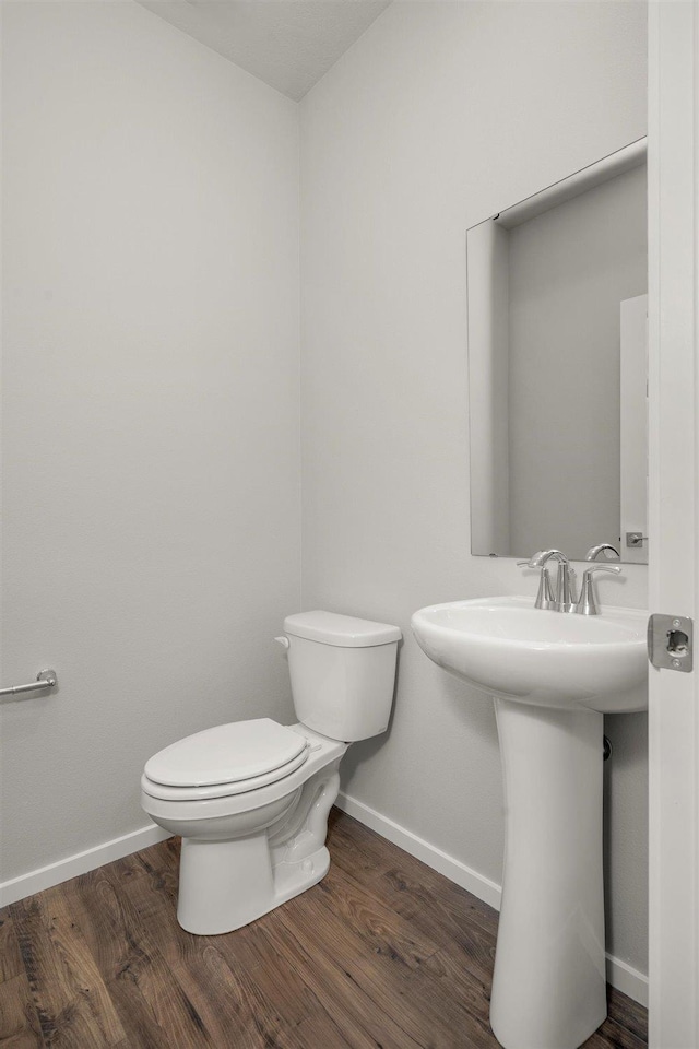 half bath with toilet, wood finished floors, baseboards, and a sink