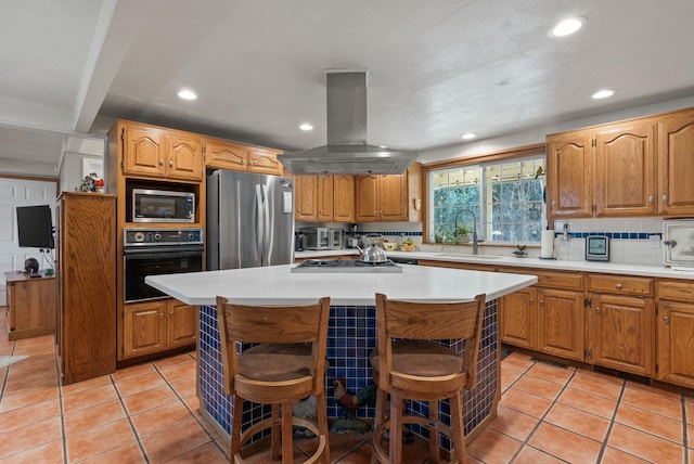 kitchen featuring light countertops, decorative backsplash, appliances with stainless steel finishes, island range hood, and a sink