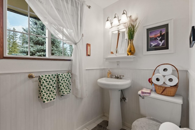 bathroom with tile patterned floors, a wainscoted wall, toilet, and a sink