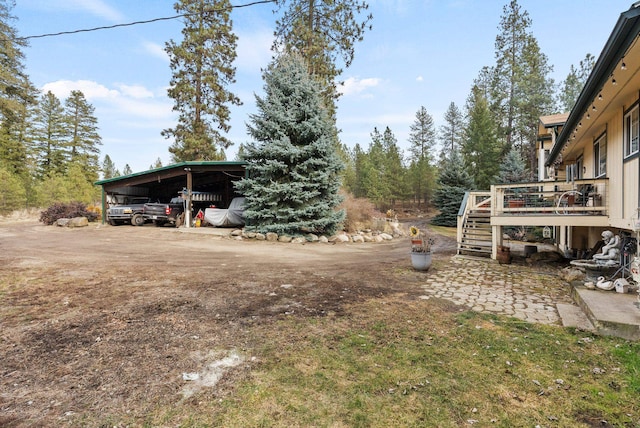 view of yard featuring stairway, a carport, a deck, and dirt driveway