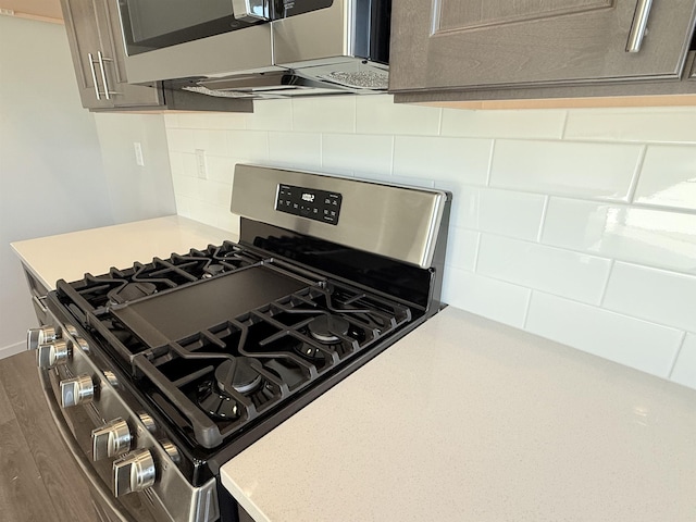 kitchen with tasteful backsplash, appliances with stainless steel finishes, light countertops, and dark wood-style flooring