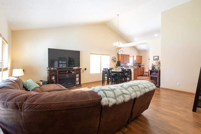 living room with a notable chandelier, light wood finished floors, and high vaulted ceiling