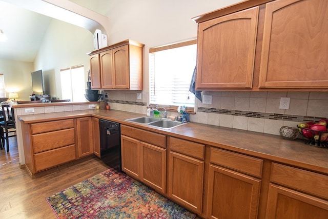 kitchen with a sink, black dishwasher, a peninsula, decorative backsplash, and vaulted ceiling