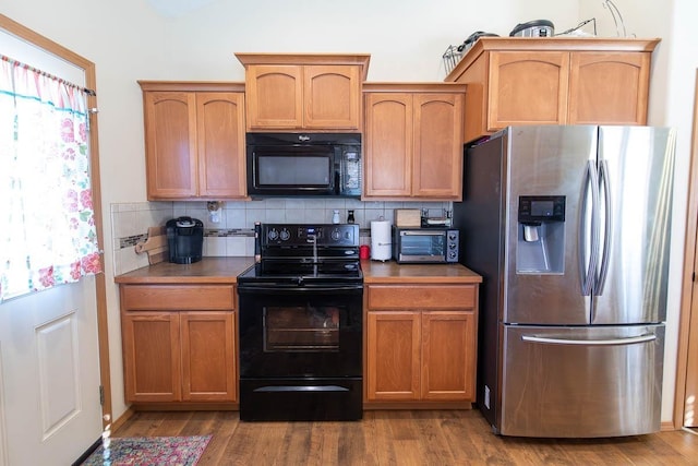 kitchen featuring plenty of natural light, backsplash, black appliances, and wood finished floors