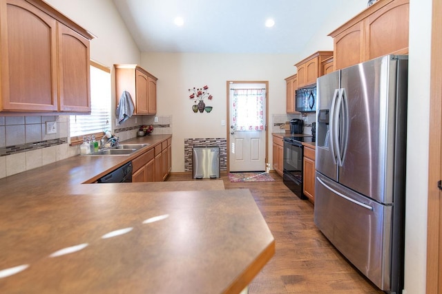 kitchen with dark wood finished floors, a sink, decorative backsplash, black appliances, and vaulted ceiling