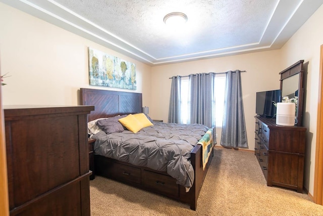 bedroom with a tray ceiling, light carpet, and a textured ceiling