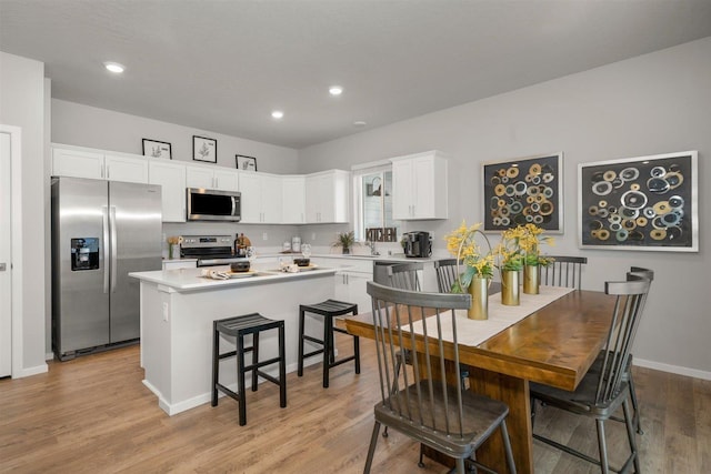 kitchen with a kitchen island, stainless steel appliances, light countertops, white cabinets, and light wood-style floors