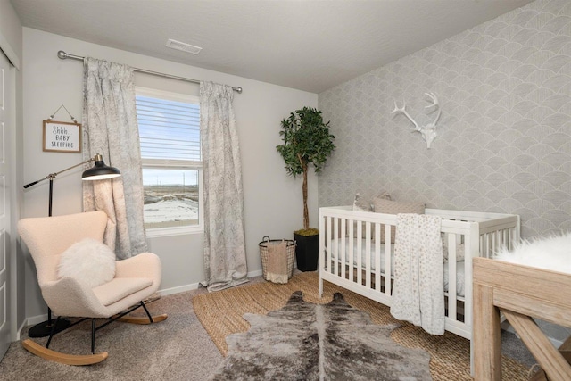 carpeted bedroom with baseboards, visible vents, wallpapered walls, a crib, and an accent wall